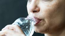 Eine schwitzende Frau trinkt Wasser. - Foto: iStock / simarik