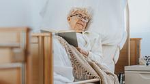 Eine alte Frau liegt mit Buch in einem Bett. - Foto: iStock / KatarzynaBialasiewicz