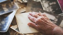 Eine alte Frau legt ihre Hand auf alte Schwarzweiß-Fotografien. - Foto: iStock/Branimir76