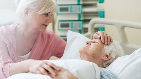 Frau tröstet Patientin mit Demenz im Endstadium im Bett - Foto: iStock/PIKSEL