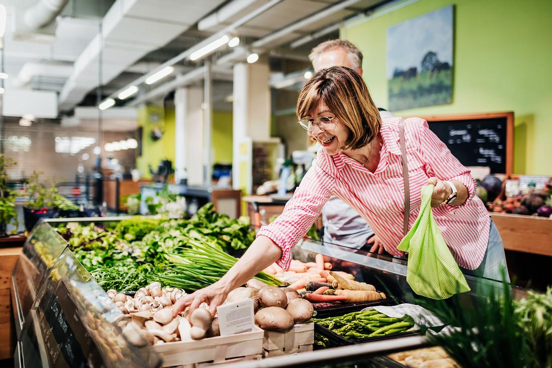 Eine ältere Frau kauft frisches Gemüse ein.