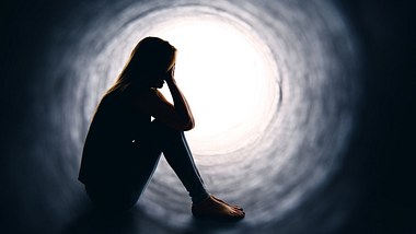 Eine depressive Frau sitzt alleine in einem Tunnel - Foto: istock_sdominick