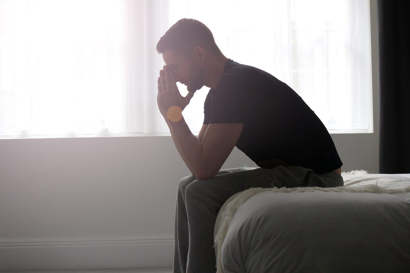 Mann hat depressive Symptome und sitzt auf der Bettkante