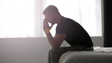 Mann hat depressive Symptome und sitzt auf der Bettkante - Foto: iStock/glegorly
