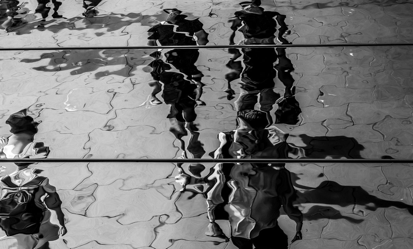 Fußgänger spiegeln sich in einer Wasserpfütze auf einem Gehweg