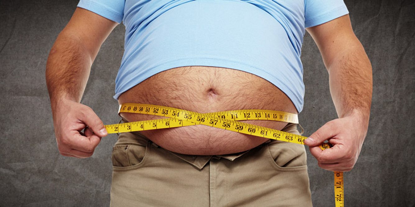 Ein dicker Mann misst seinen Bauchumfang mit einem Maßband