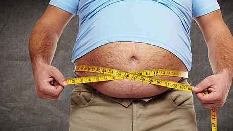 Ein dicker Mann misst seinen Bauchumfang mit einem Maßband - Foto: Fotolia