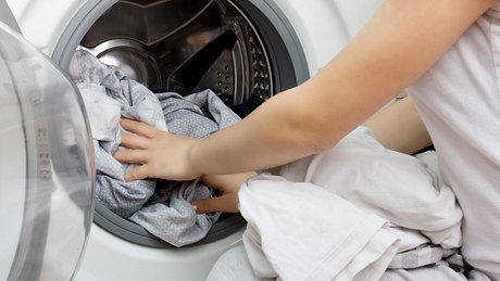 Frau legt Wäsche in die Waschmaschine. - Foto: iStock/Yana Tikhonova
