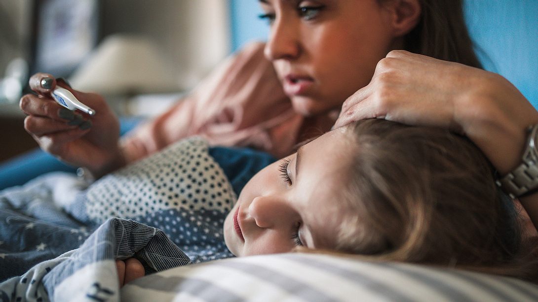 Kind liegt krank im Bett, Mutter misst Fieber - Foto: iStock-1216399995 zeljkosantrac