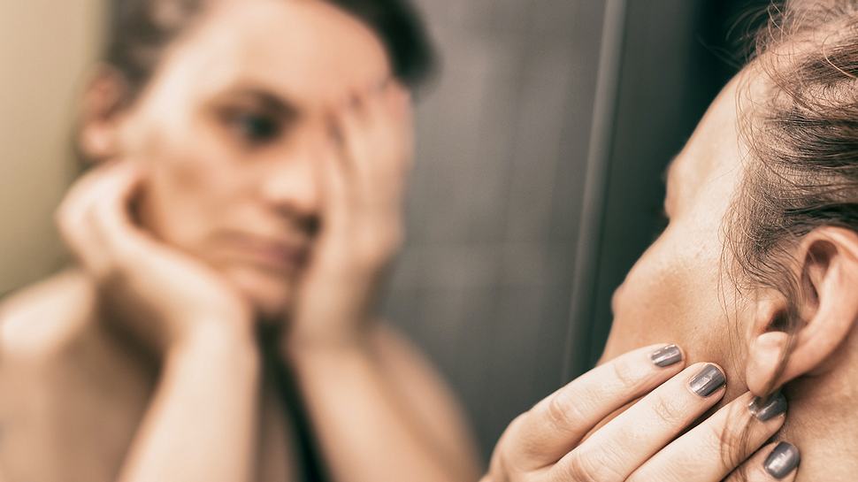 Frau mit Dysmorphophobie blickt in den Spiegel - Foto: iStock/MarinaZg