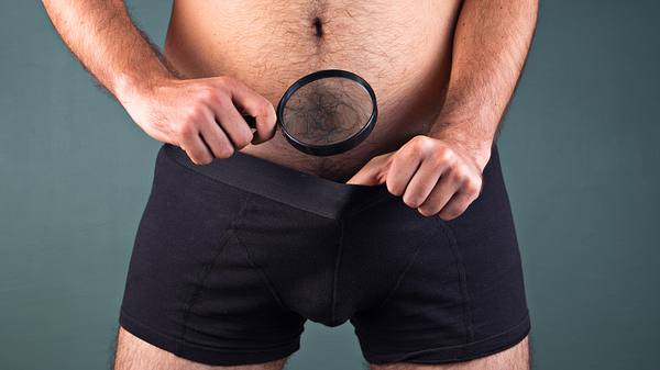 Mann schaut mit Lupe seinen Penis an - Foto: iStock/themacx