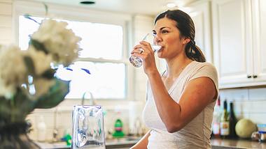 Eine Frau steht in der Küche und trinkt Wasser - Foto: istock_eyecrave