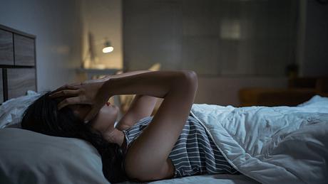 Frau liegt wach im Bett und hält sich die Hände an den Kopf - Foto: iStock/torwai