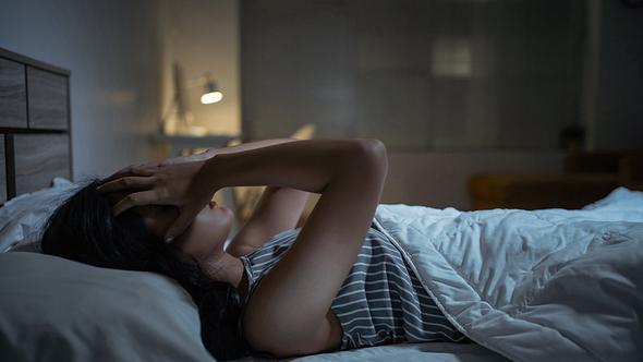 Frau liegt wach im Bett und hält sich die Hände an den Kopf - Foto: iStock/torwai