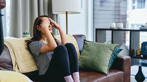 Frau auf dem Sofa mit Kopfschmerzen - Foto: iStock/Charday Penn