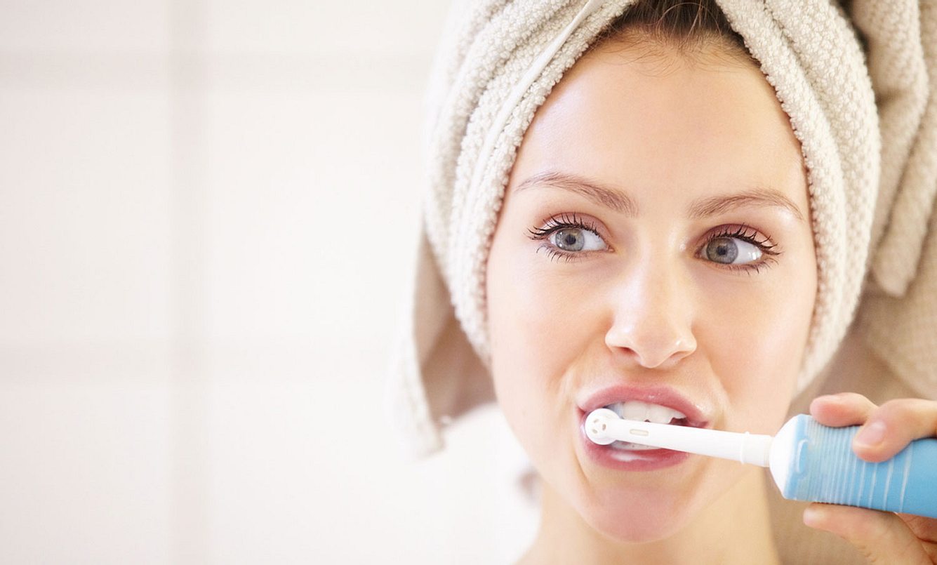 Eine Frau putzt sich die Zähne mit einer elektrischen Zahnbürste