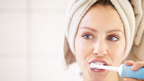 Eine Frau putzt sich die Zähne mit einer elektrischen Zahnbürste - Foto: PeopleImages/iStock