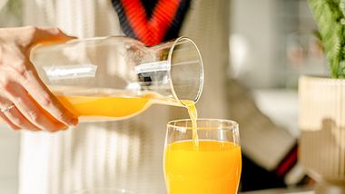 Ein Mann gießt Orangensaft in eine Karaffe - Foto: iStock/Jokic