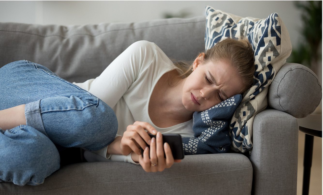 Eine Frau liegt mit ihrem Smartphone auf dem Sofa und weint