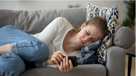 Eine Frau liegt mit ihrem Smartphone auf dem Sofa und weint - Foto: iStock/﻿fizkes