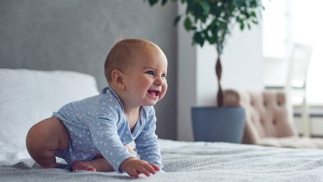 Ein Baby krabbelt auf einem Bett - Foto: iStock/sandsun