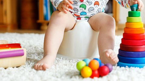 Kleinkind auf dem Töpfchen; es steht auf einem Teppich, Spielzeug liegt daneben - Foto: iStock-929584544 romrodinka