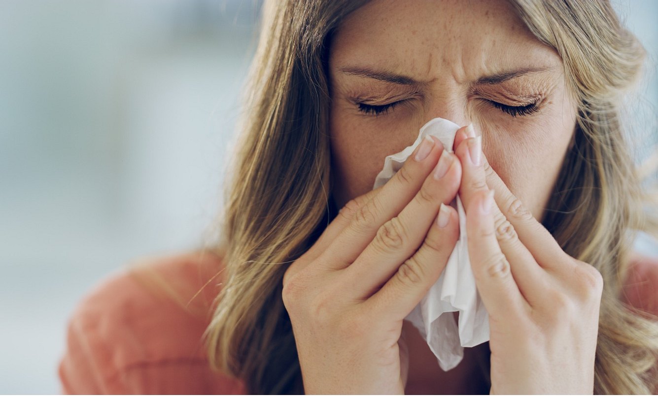 Eine erkältete Frau schnäuzt ihre Nase
