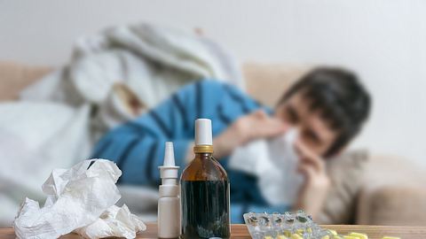 Mann liegt auf dem Sofa und putzt sich die Nase; im Vordergrund Medikamente - Foto: iStock/vchal