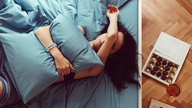 Depressive Frau liegt mit Schokolade und Alkohol im Bett - Foto: iStock / Martin Dimitrov