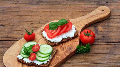 Vollkornbrot mit Quark, Gurken und Tomaten auf einem Holzbrett - Foto: iStock-612236942 juefraphoto