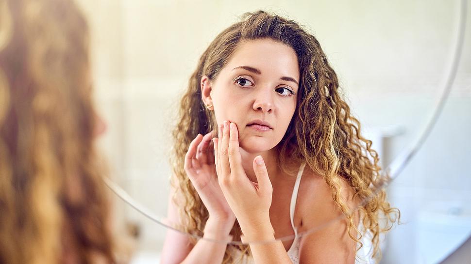 Frau untersucht ihr Gesicht auf Pickel und Unreinheiten - Foto: istock | Charday Penn