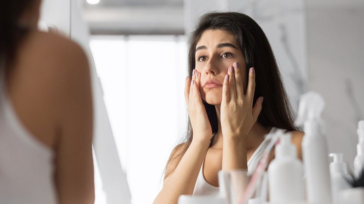 Eine Frau begutachet ihre Haut im Spiegel - Foto: istock_Prostock-Studio