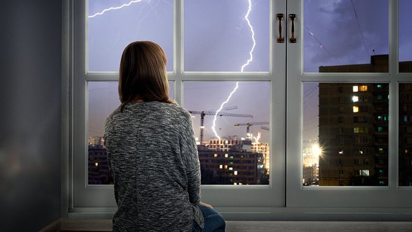 Frau sitzt während eines Gewitters am Fenster - Foto: iStock/ kozorog