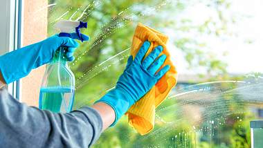 Person mit Handschuhen beim Fensterputzen mit Sprühflasche und Tuch - Foto: istock/AlexRaths