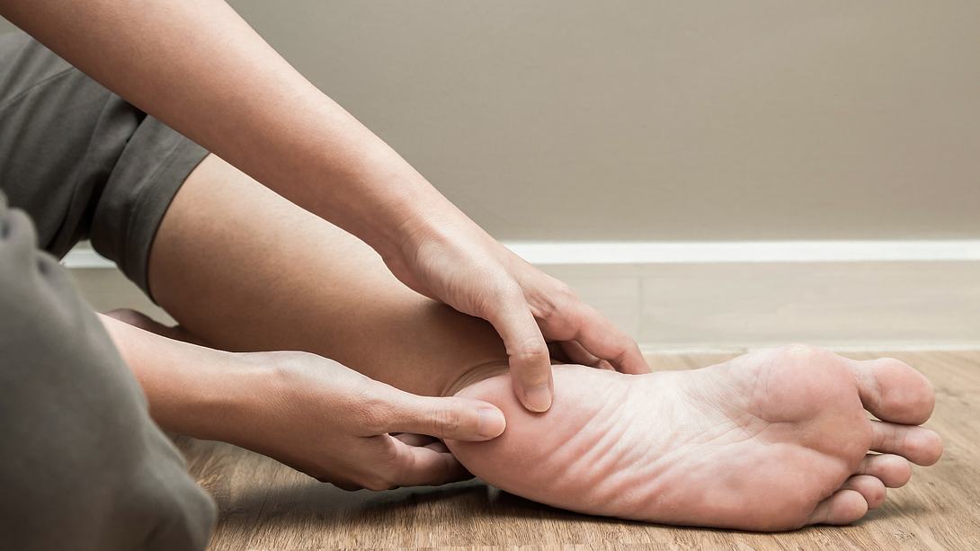 Frau hält sich schmerzenden Fuß mit Fersensporn - Foto: iStock/catinsyrup