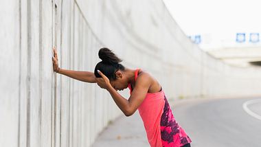 Frau in Sportkleidung stützt sich gegen Wand und hält sich den Kopf - Foto: iStock/piranka