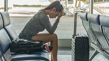 Eine Frau sitzt im Flughafenwartebereich und hält sich besorgt den Kopf. - Foto: iStock / globalmoments