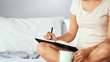 Frau schreibt etwas in ein Buch im Bett - Foto: iStock/LaylaBird