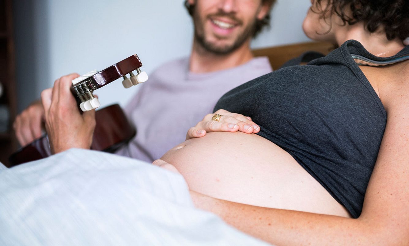 Mann spielt schwangerer Frau etwas auf der Gitarre vor