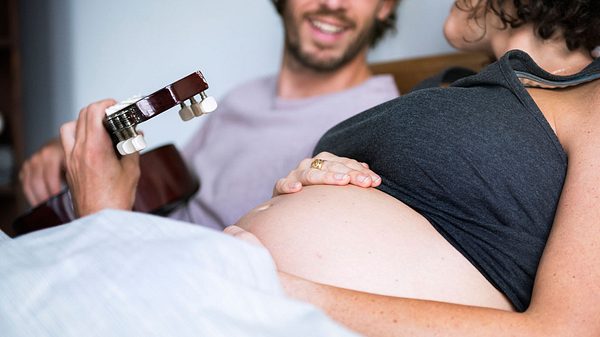 Mann spielt schwangerer Frau etwas auf der Gitarre vor - Foto: iStock/Rawpixel