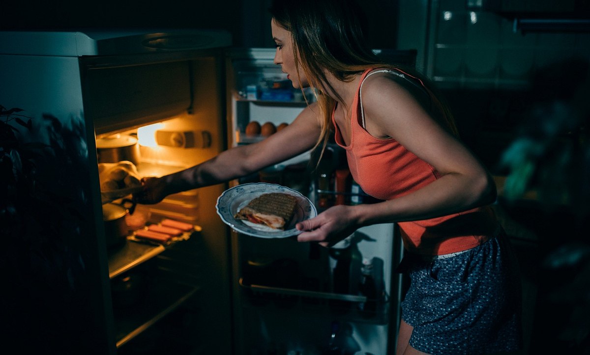 Frau holt sich abends essen aus dem Kühlschrank