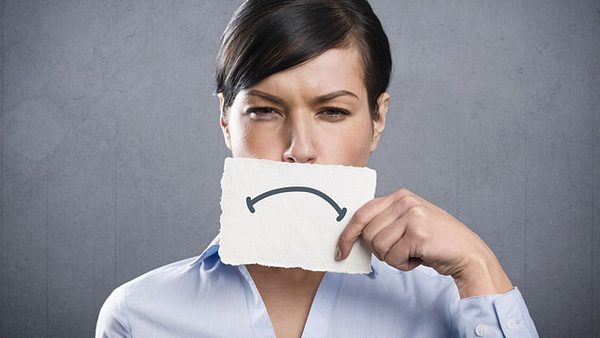 Eine Frau hält sich einen Zettel mit einem traurigen Mund vors Gesicht - Foto: Fotolia