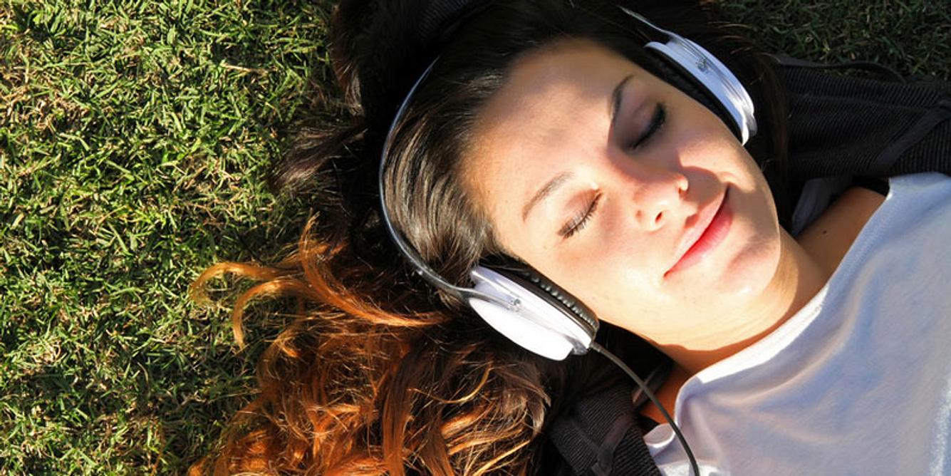 Eine Frau liegt im Gras und hört Musik