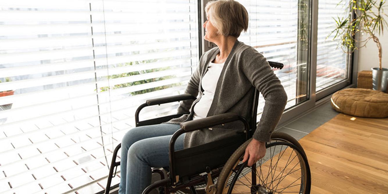 Frau im Rollstuhl guckt aus dem Fenster