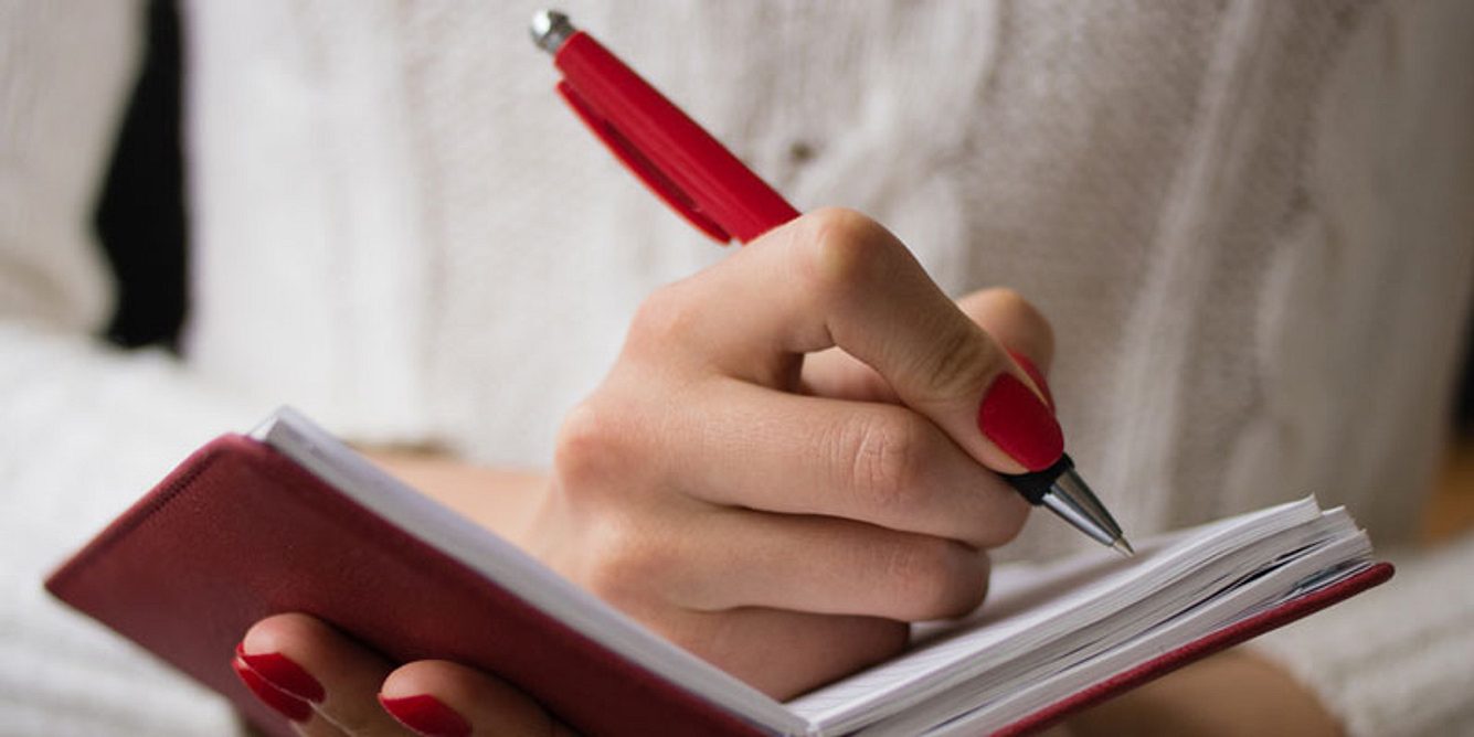 Frau schreibt in rotes Notizbuch