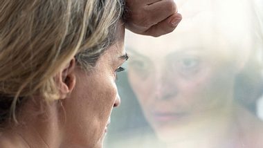 Traurige Frau lehnt am Fenster - Foto: iStock/Juanmonino