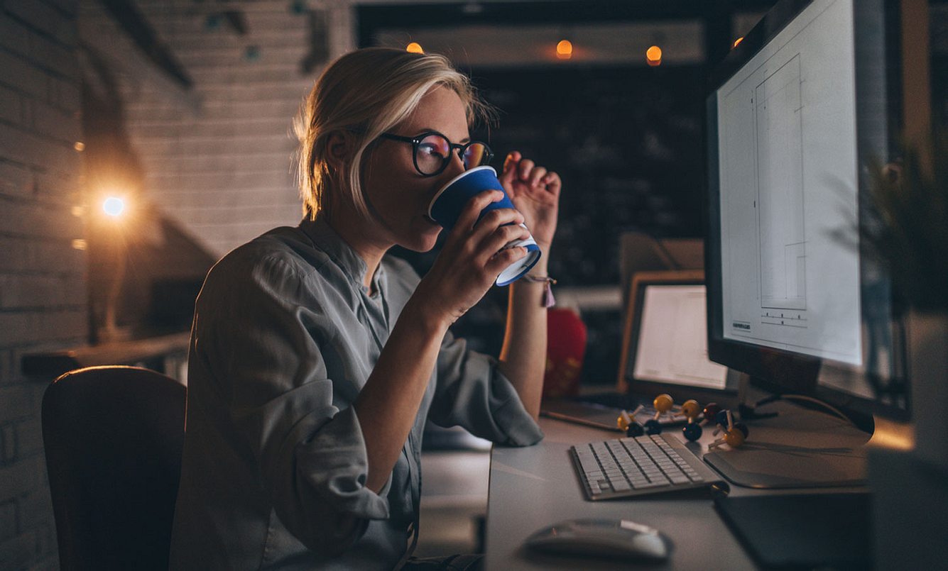 Eine Frau trinkt abends Kaffee am Computer