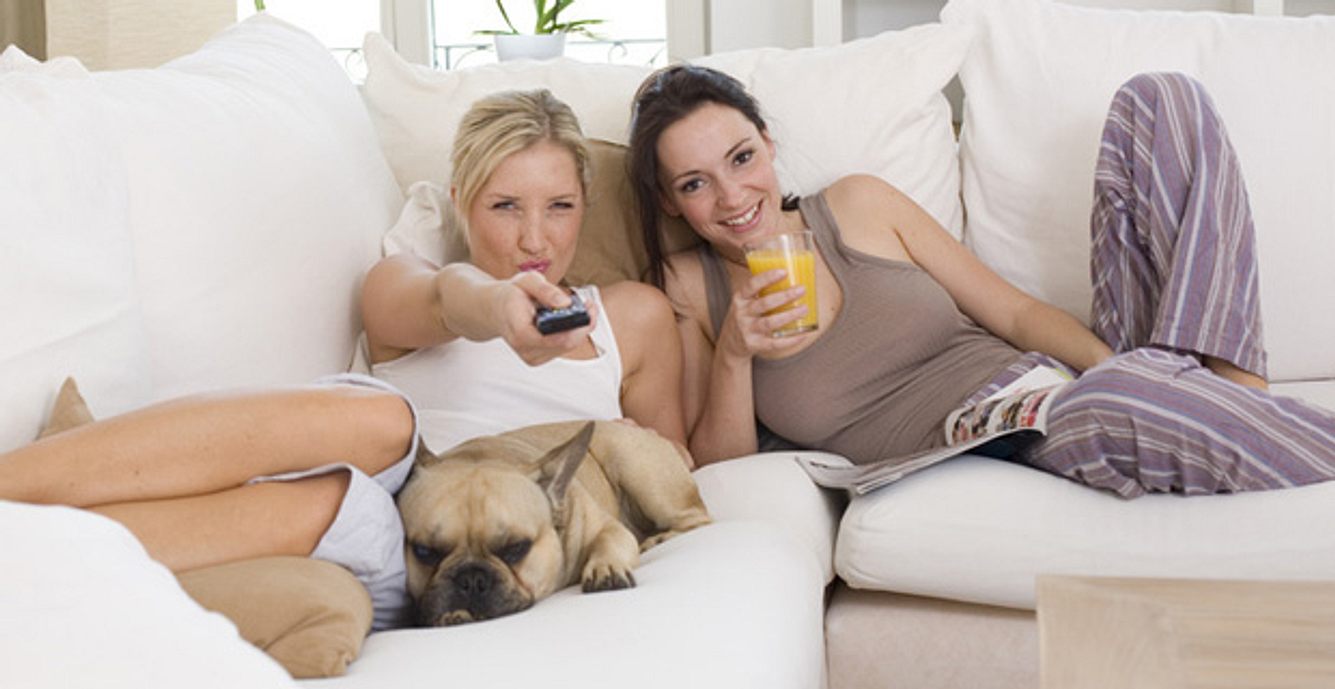 Zwei Freundinnen sitzen auf einer Couch und sehen fern