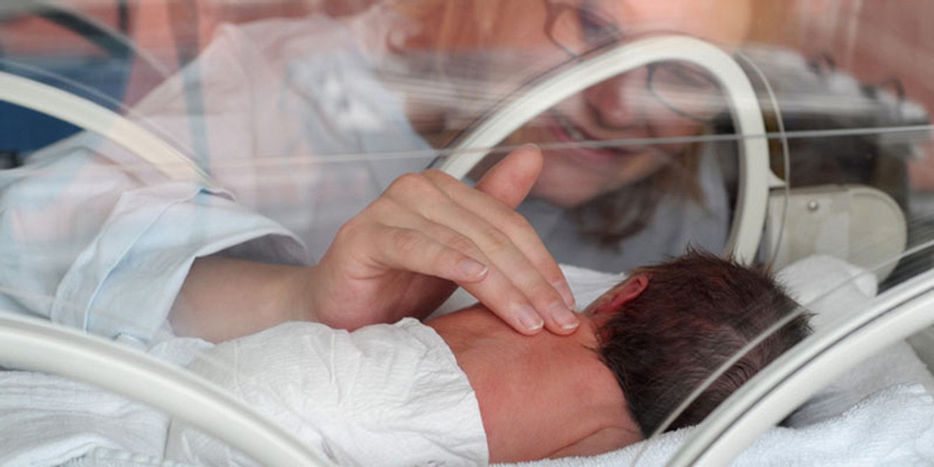 Eine Mutter streichelt ihr Frühchen im Brutkasten