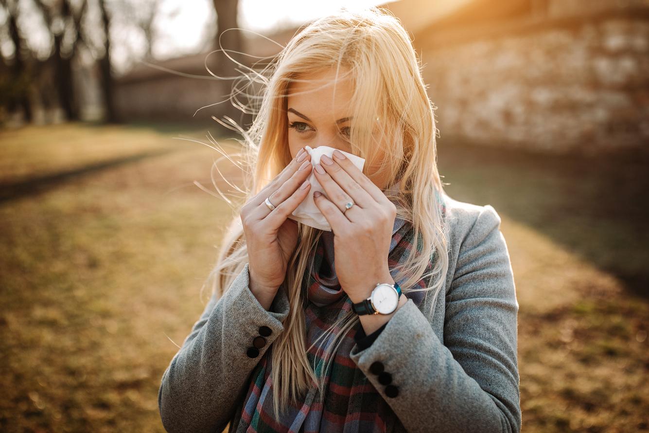 Frau mit Frühblüher-Allergie putzt sich die Nase mit einem Taschentuch